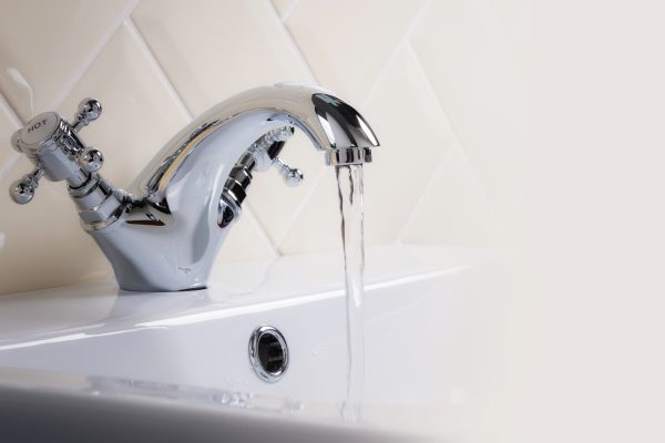 A closeup shot of water flowing from a basin mixer tap in the bathroom